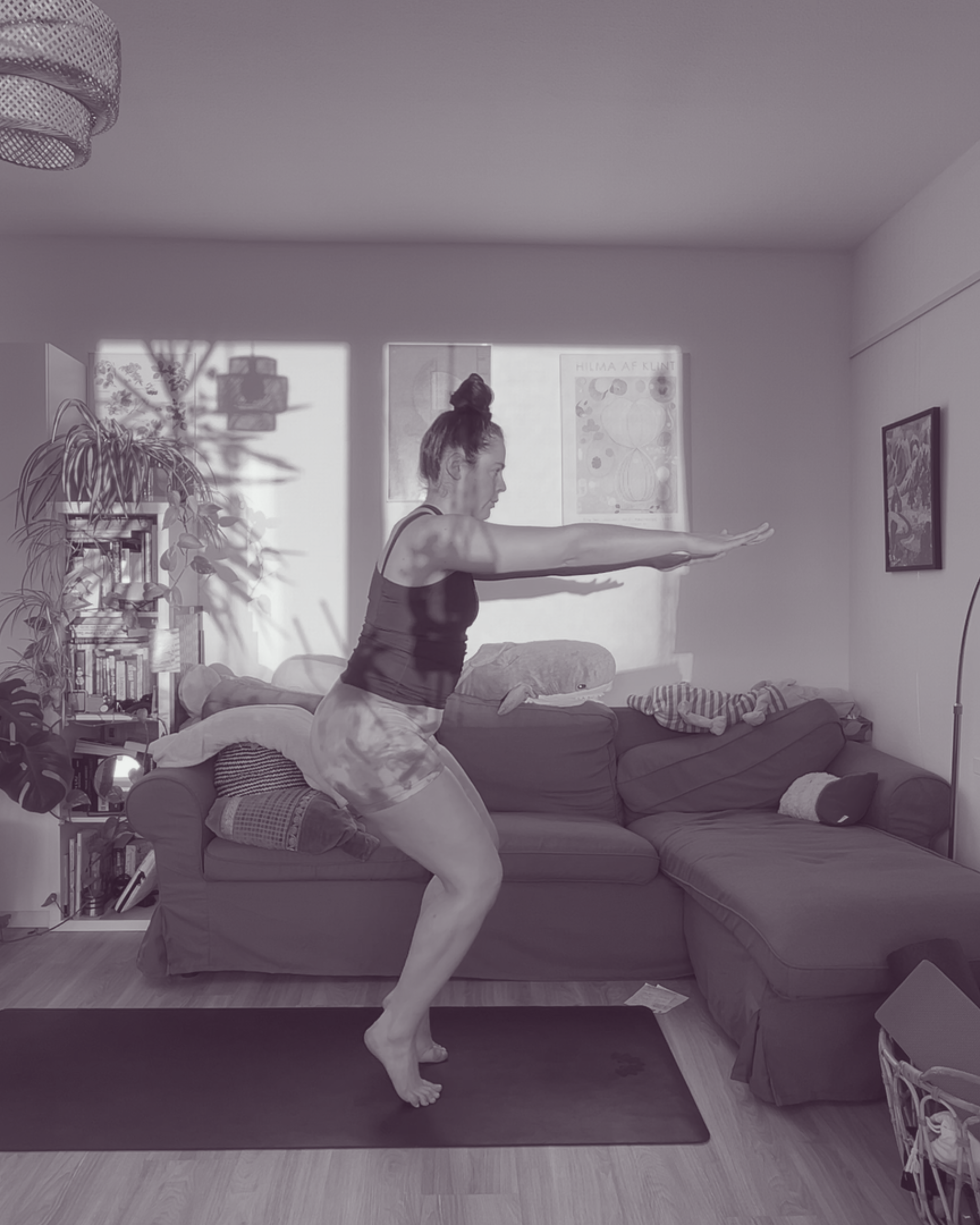 Frau in Sportkleidung übt im Wohnzimmer eine tiefe Balanceposition auf einem Bein mit nach vorne gestreckten Armen